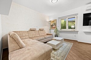 Un salon moderne avec un canapé d’angle, une table basse, une plante en pot et une grande fenêtre offrant une belle vue.