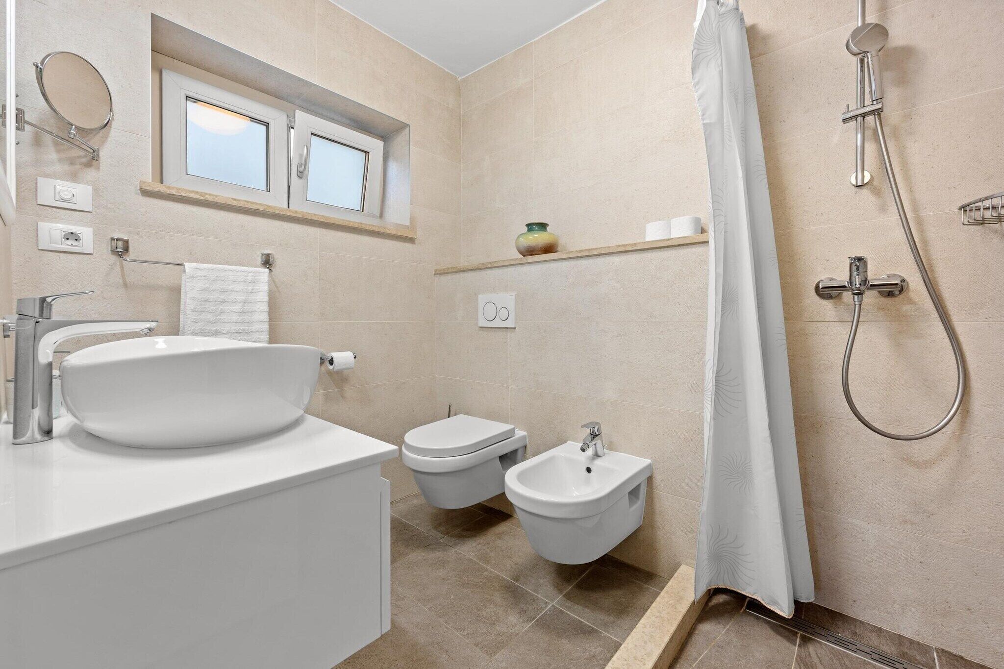 Un baño moderno con un lavamanos grande blanco, un bidé, un inodoro y una ducha.