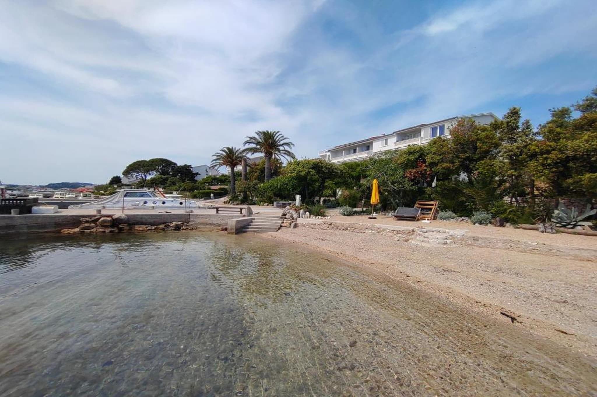 Eine Küstenregion mit klarem Gewässer, einem Sandstrand und einem Gebäude mit Balkon mit Blick aufs Wasser.