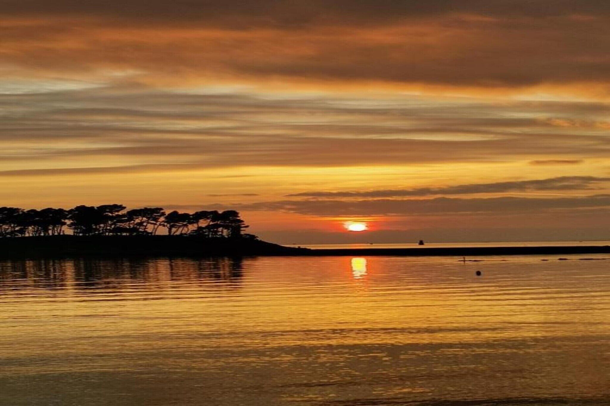 Un atardecer sobre un cuerpo de agua tranquilo, con la silueta de árboles en el horizonte.
