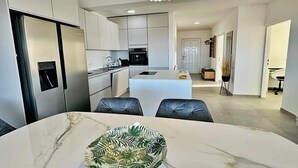 A modern kitchen with white cabinets, a central island, and a dining area with a marble table. - Spacious apartment with wonderful sea view (Banjol)