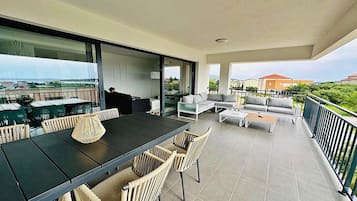 A spacious balcony with a dining area, seating, and a view of the sea.