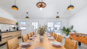 A modern dining room with a wooden table set for six, surrounded by wooden chairs. There is a foosball table to the right and a large window providing natural light. - Lovely family bungalow with private pool (Valbandon)