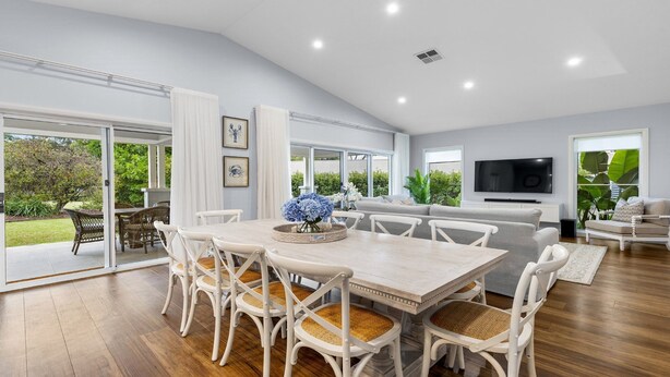 A spacious living area with a dining table, white chairs, a sofa, and a television.