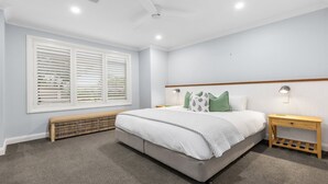 A bedroom with a large bed, a bench, two bedside tables, and a ceiling fan.