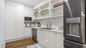 A modern kitchen with white cabinetry, a stainless steel refrigerator, a built-in microwave, a sink with a faucet, and a water dispenser.