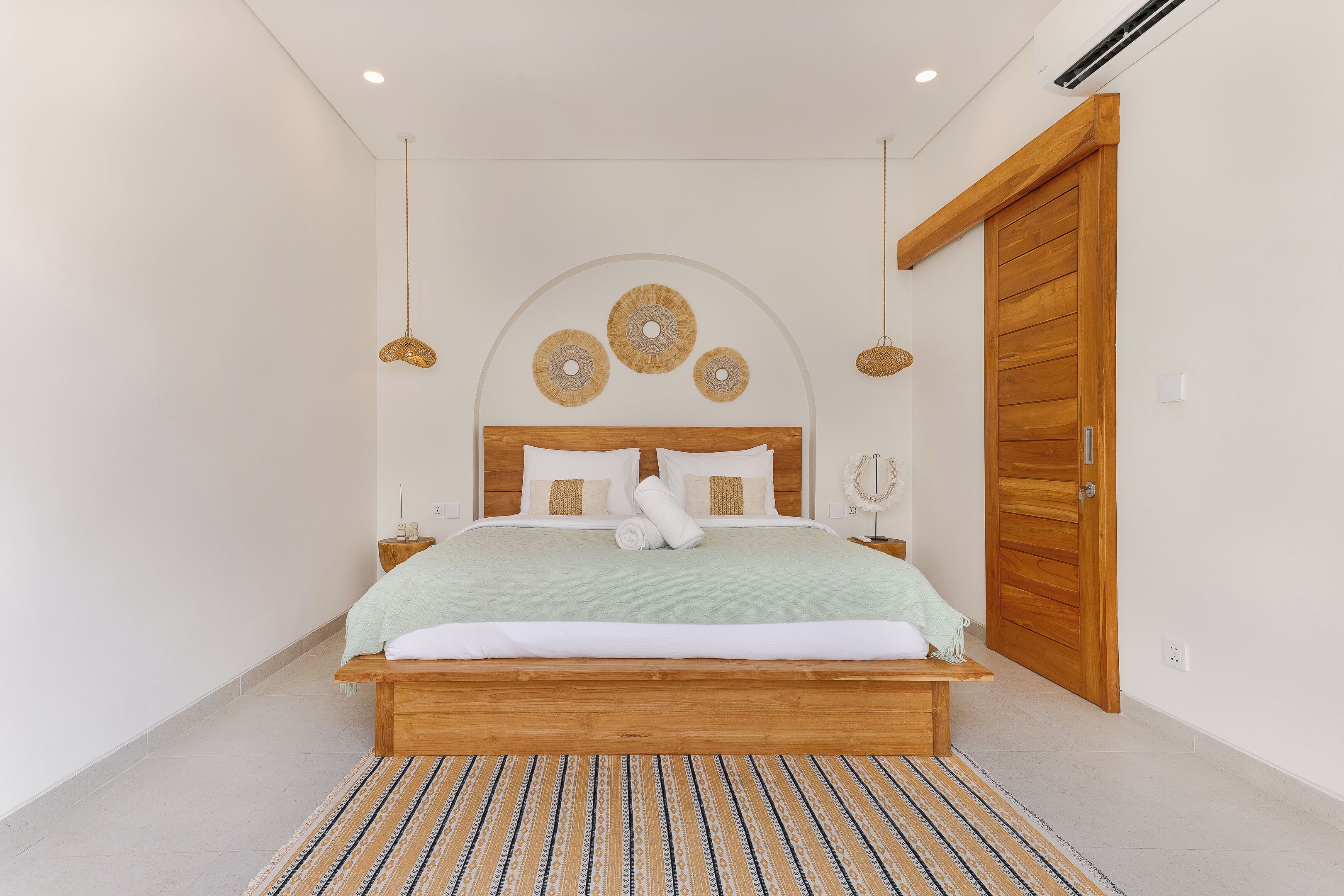 Une chambre avec un lit en bois, un tapis à motifs et une porte en bois.