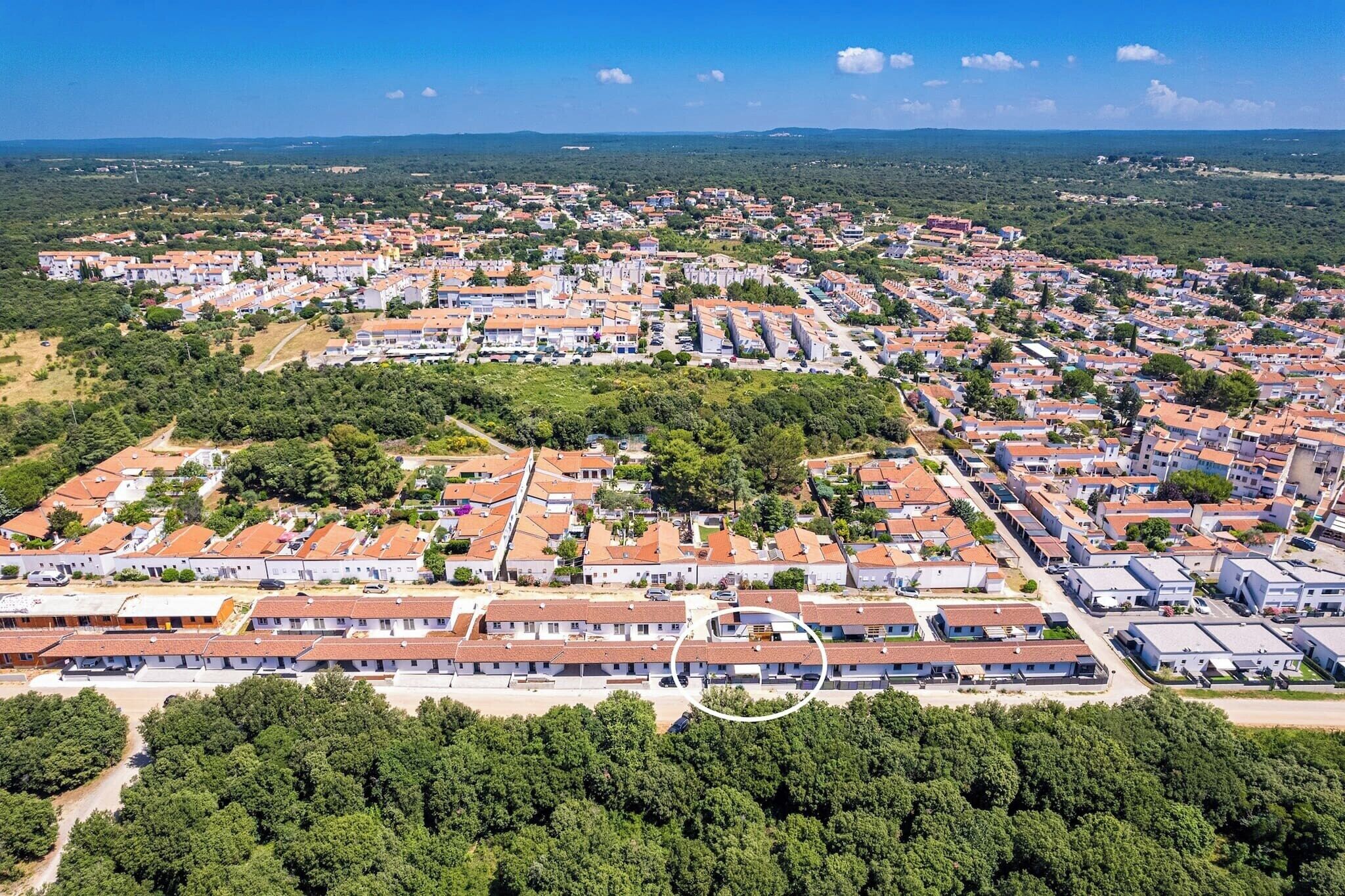 An aerial view of a residential area with uniform houses, green spaces, and a clear sky.