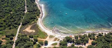 Vista aérea de una zona costera con playa, bosque denso y aguas azules cristalinas.