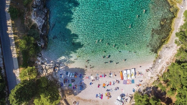 An aerial view of a beach with clear turquoise water, a sandy shore, and several beach umbrellas and sun loungers. - Apartment, 100m from the beach (Peroj)