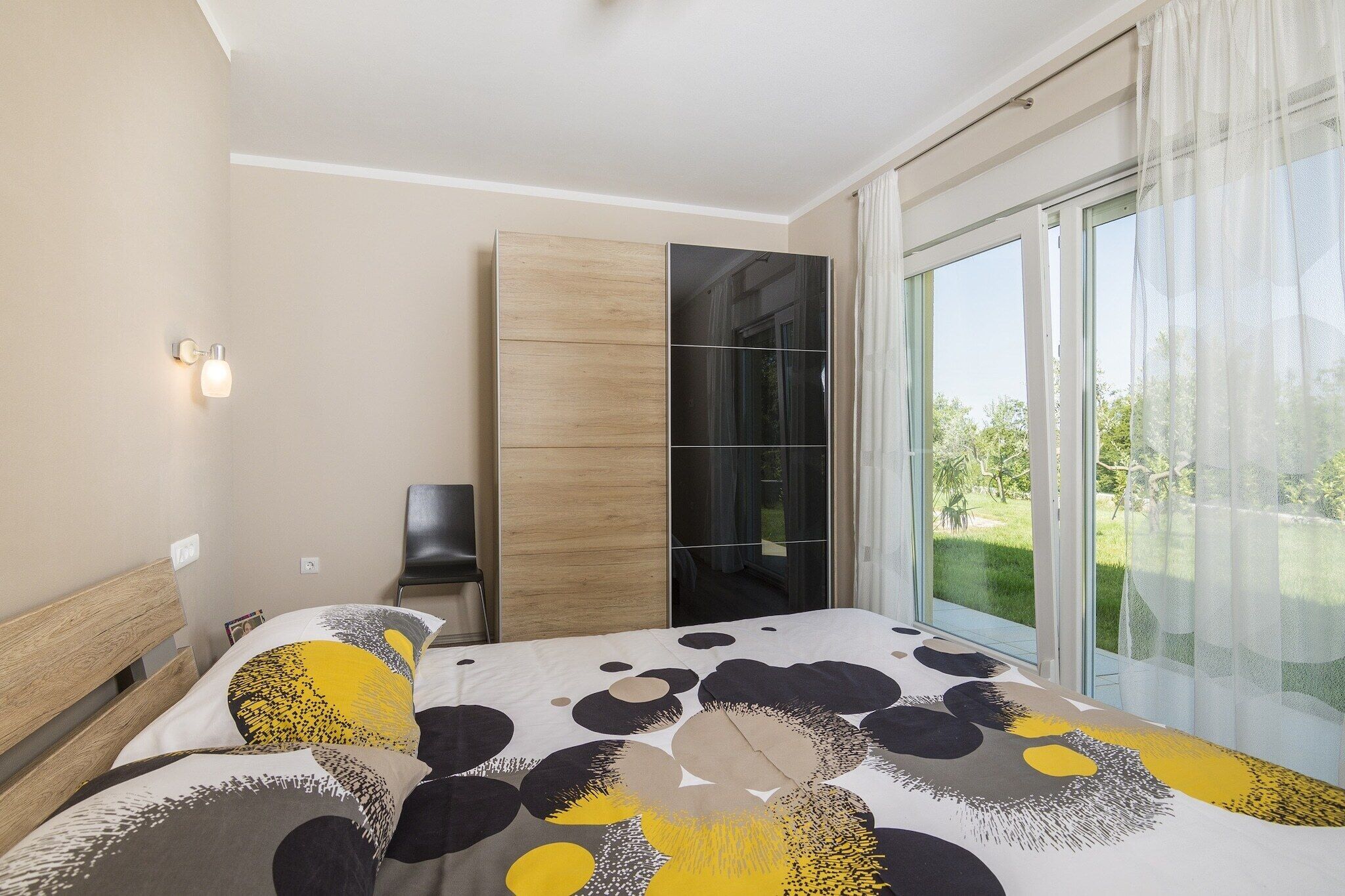 A modern bedroom with a large bed, a built-in wardrobe, and a sliding glass door leading to a balcony.