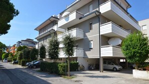 A multi-story residential building with balconies, a parking area, and a clear sky. - Bright escape near the beach (Bibione)