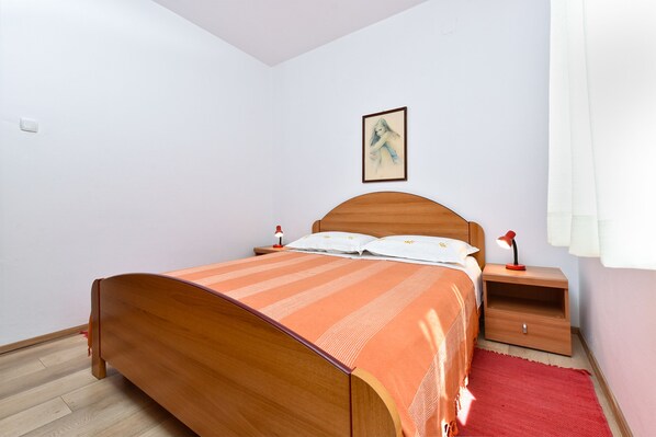 A bedroom with a wooden bed, a nightstand with a lamp, a red rug, and a framed picture on the wall.