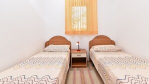 Una habitación con dos camas individuales, una mesita de noche con lámpara y una ventana con cortina.