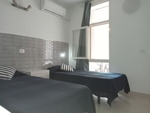 Une chambre avec deux lits, une fenêtre avec des rideaux, un miroir et un appareil de climatisation.