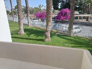 A balcony with a view of a parking area, palm trees, and a fence.
