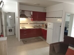 Una cocina compacta con armarios rojos, un refrigerador blanco, una lavadora y un lavamanos.