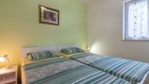 A bedroom with two beds, a bedside table with a lamp, a framed picture on the wall, and a window with curtains. - Apartment in Labin near Rabac Beaches (Labin)