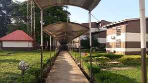Ein überdachter Gang mit einem Betonweg, gesäumt von Grünflächen und Gebäuden mit roten Dächern und gestreiften Wänden.