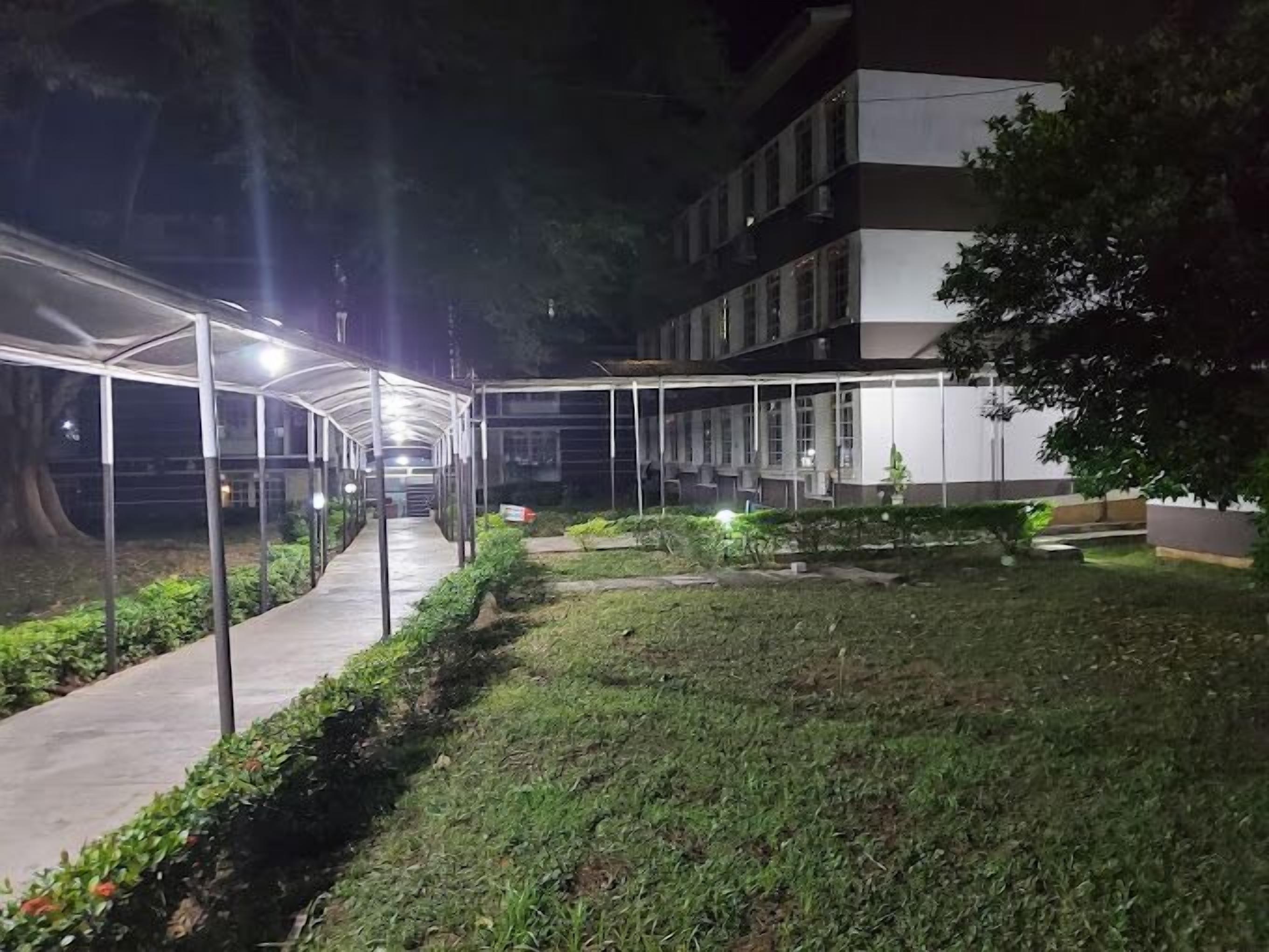 Un pasillo cubierto con techo de vidrio, rodeado de vegetación y un edificio con amplias ventanas.