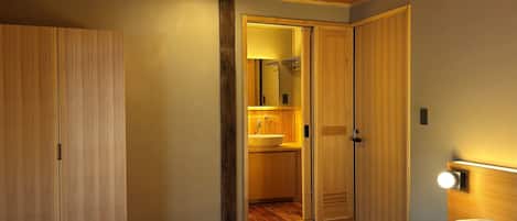 A bedroom with a wooden ceiling, a bed with white bedding, a wooden wardrobe, and a bathroom with a sink and mirror.