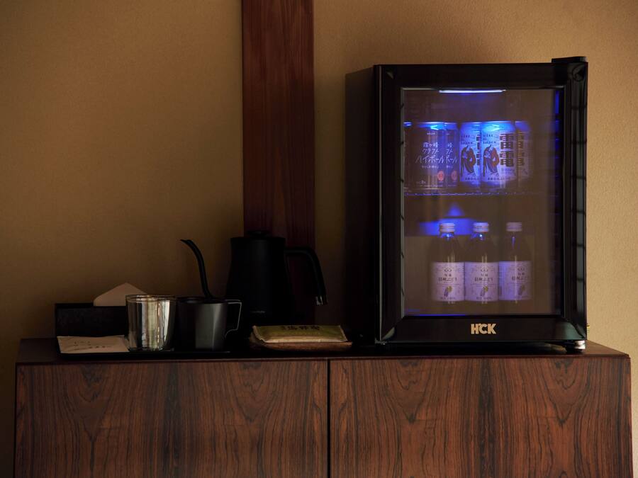 A wooden cabinet with a black HCK refrigerator displaying Japanese beverages.