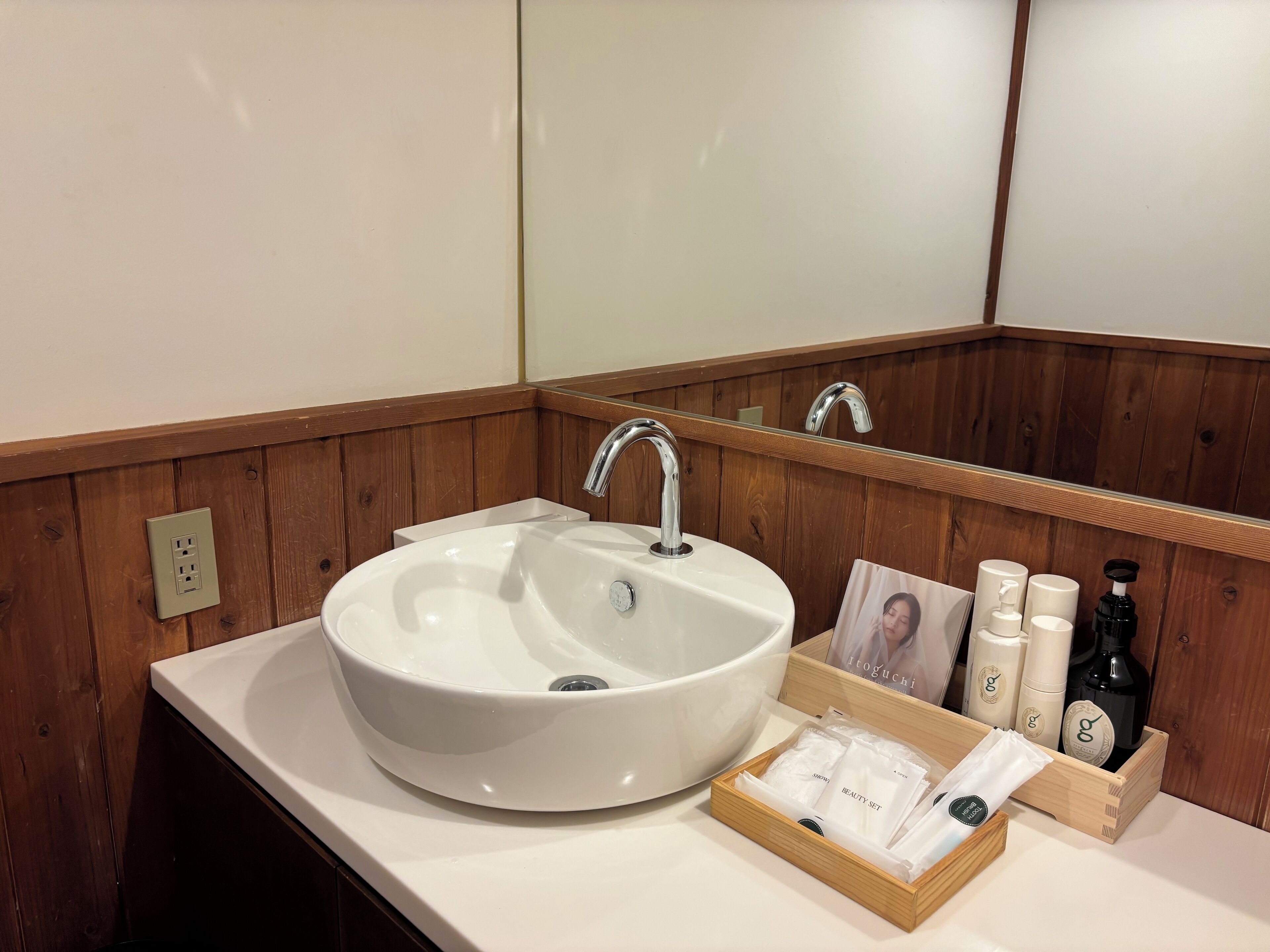 A bathroom with a white sink, wooden paneling, a mirror, and a wooden box containing toiletries.
