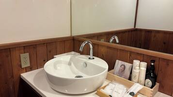 A bathroom with a white sink, wooden paneling, a mirror, and a wooden box containing toiletries.
