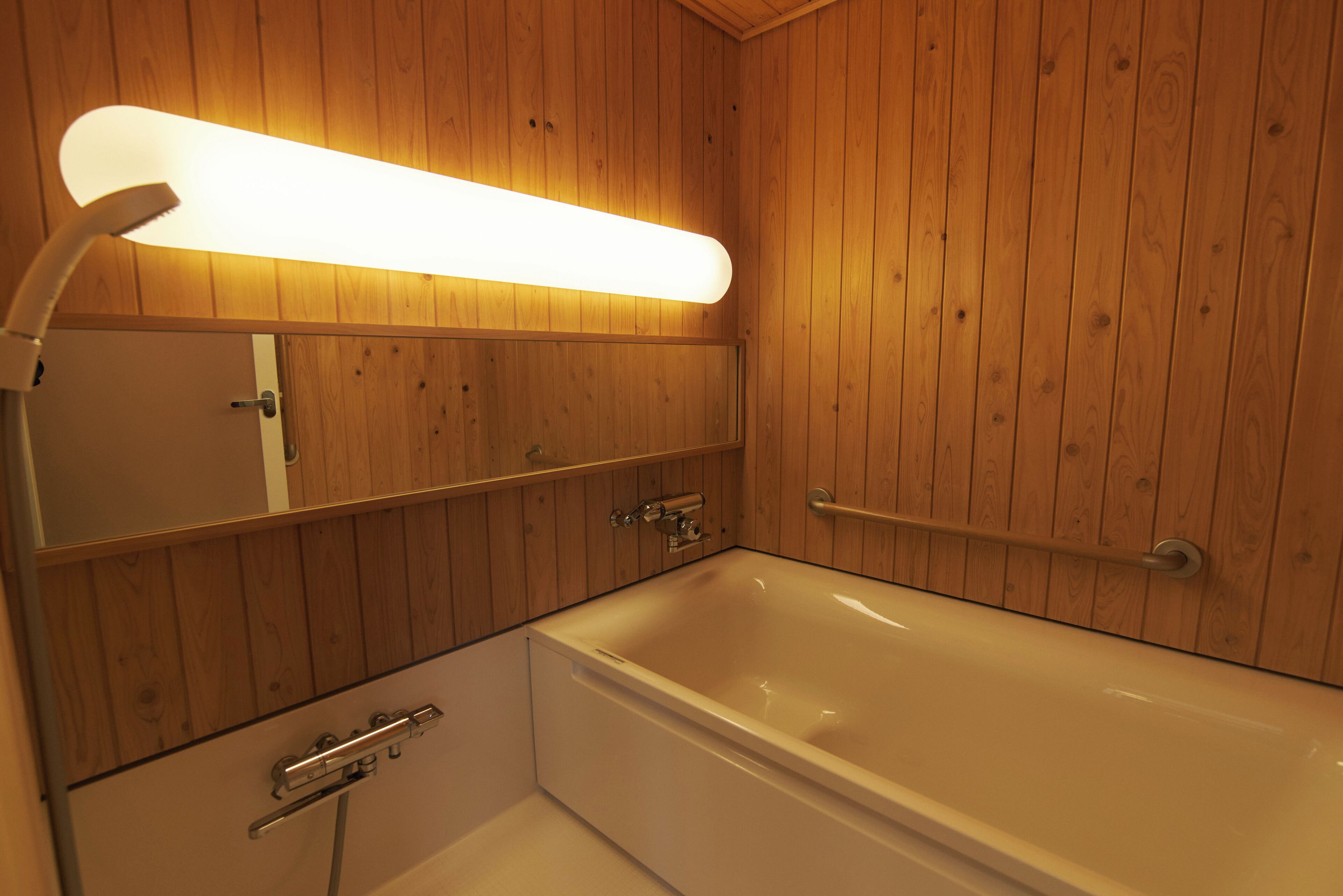 Un baño con paneles de madera, una bañera blanca, un espejo y una lámpara fijada a la pared.