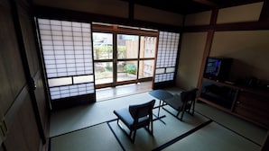 A traditional Japanese room with tatami flooring, a low table with a bench, a television, and sliding doors with a view of the outside. - Travel Stop UNNOWA (Tomi)