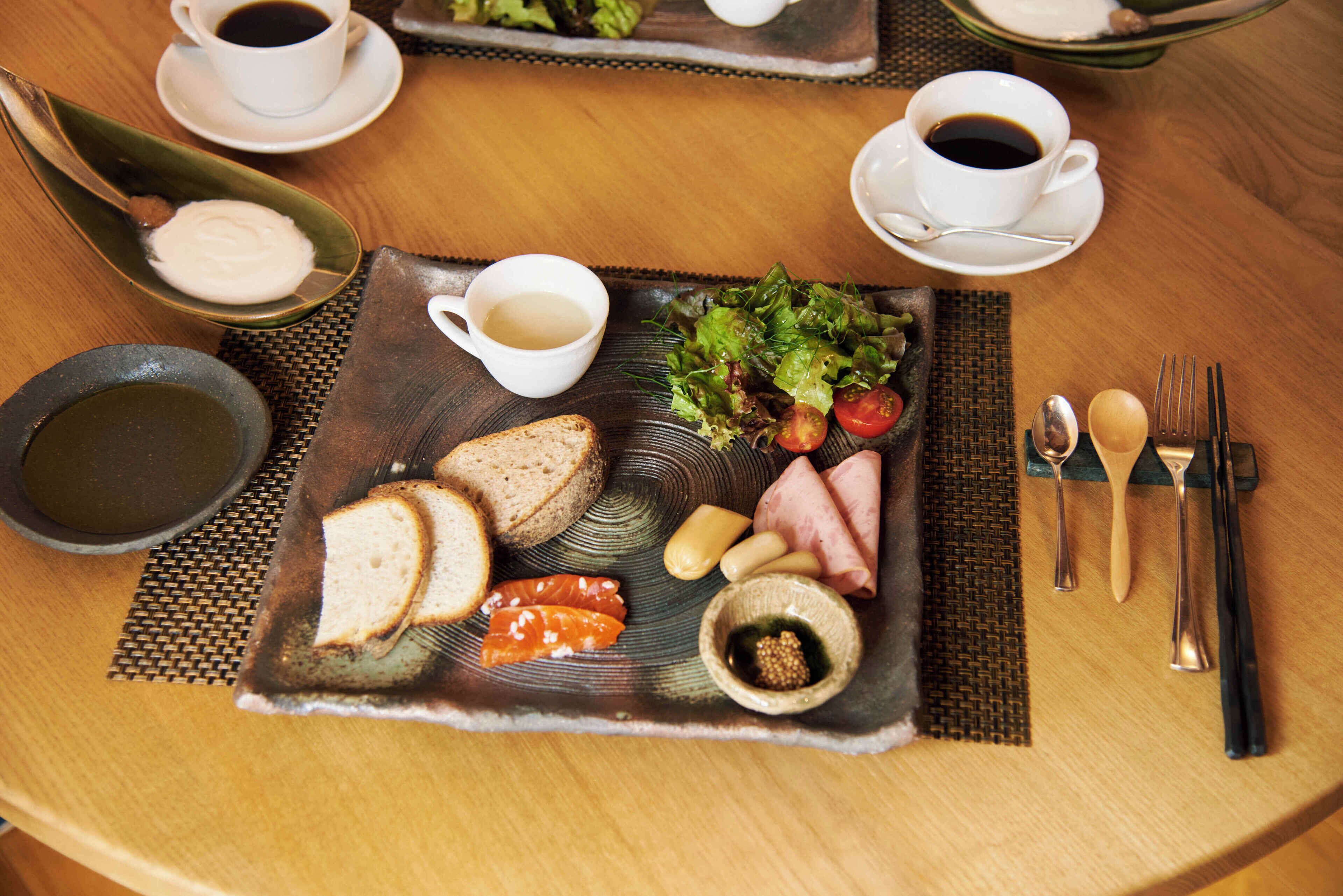 Bandeja de desayuno con pan, queso, jamón y ensalada sobre un protector de tela trenzada.