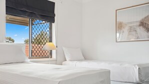 Habitación de hotel con dos camas, una ventana con persiana oscura, una lámpara y un cuadro en la pared.