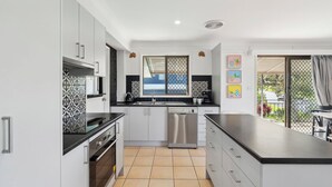 Una cocina moderna con armarios blancos, encimera negra y lavavajillas. Hay una ventana con vistas al exterior, y un balcón con vistas al jardín.