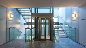 A modern interior with a glass elevator, glass railings, and a staircase leading to upper floors.