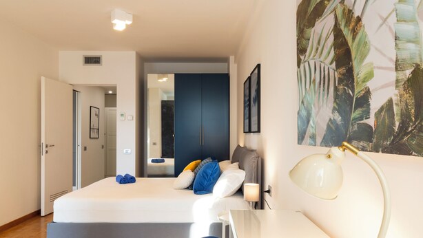 A modern bedroom with a bed, bedside table, lamp, and artwork.
