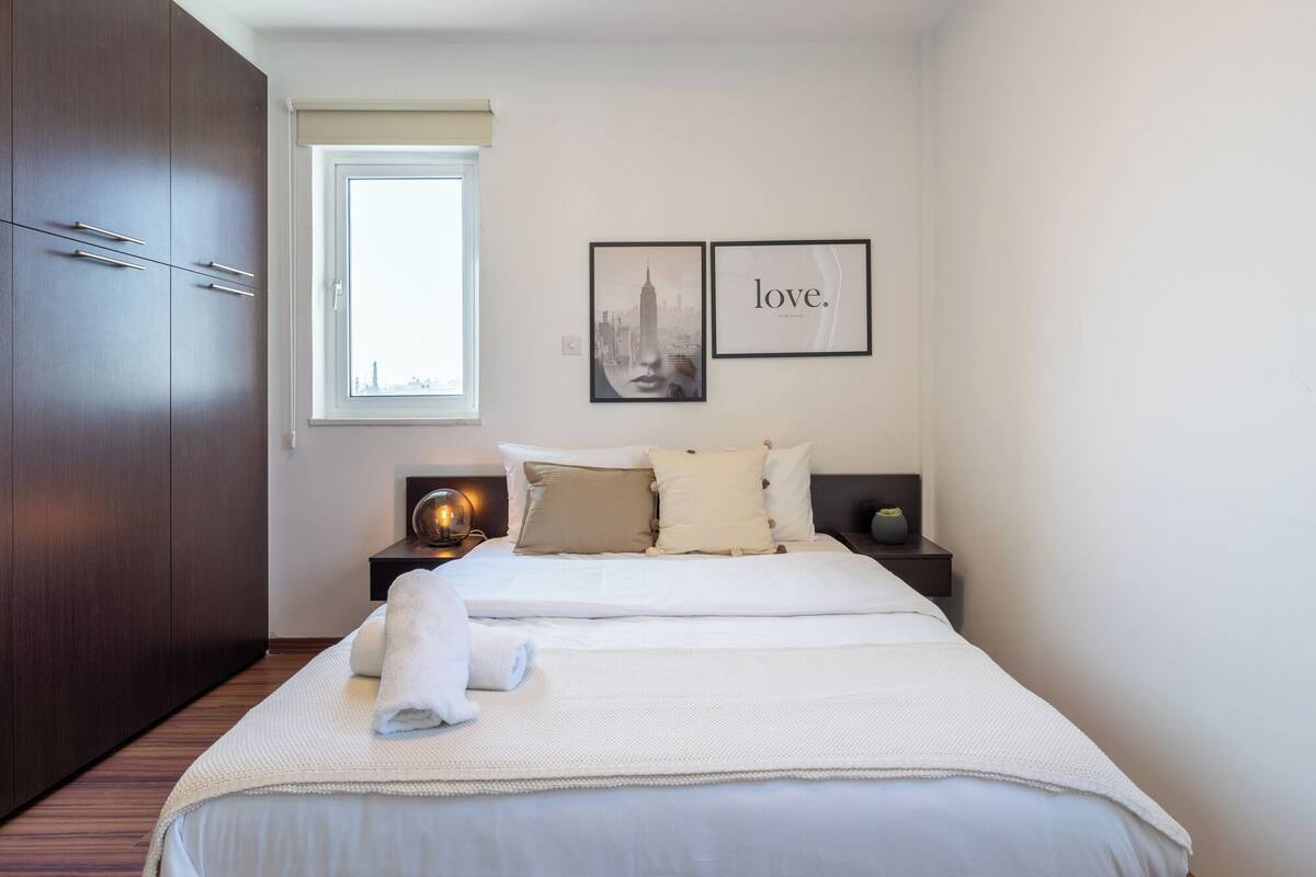 A hotel room with a large bed, a nightstand with a lamp, a wardrobe, and two framed pictures on the wall.