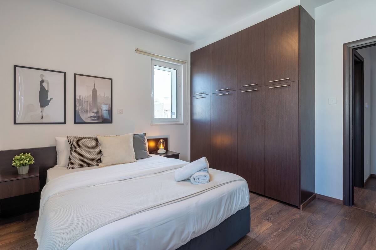 A modern bedroom with a large bed, a wardrobe, and two framed pictures on the wall.