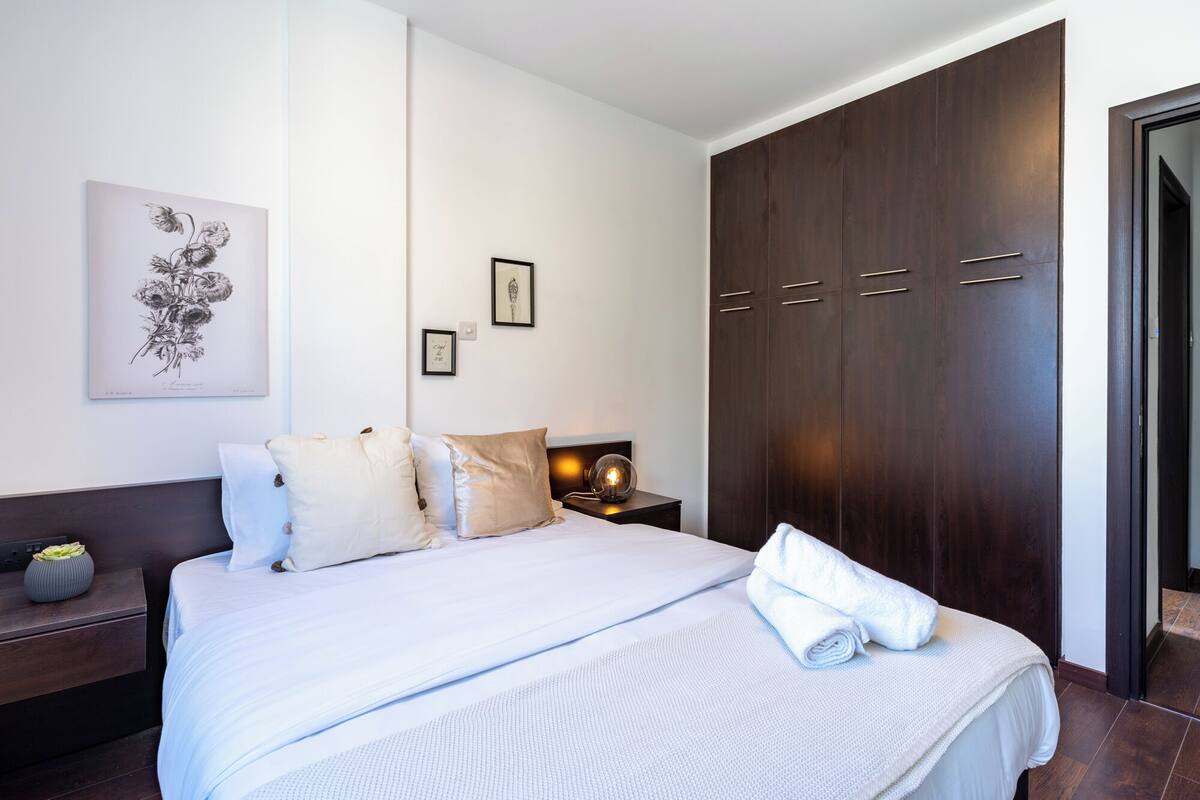 A neatly arranged bedroom with a large bed, a nightstand, a wall-mounted lamp, and a wardrobe.