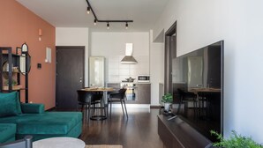 Una sala moderna con un sofá verde, un comedor con mesa y sillas, una cocina con estufa y microondas, y un televisor de pantalla plana grande.