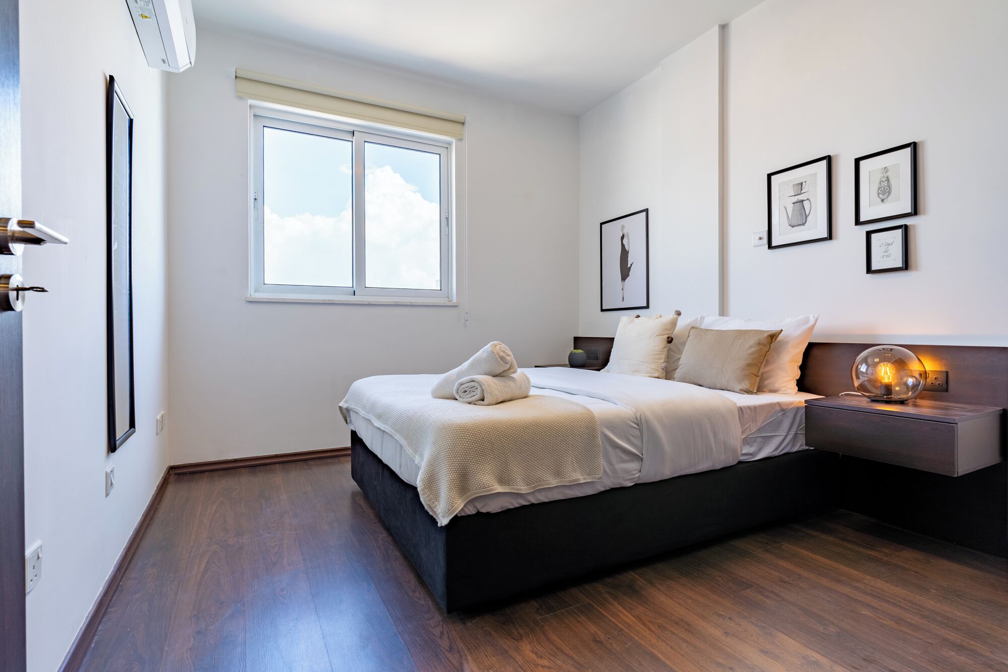 Ein modernes Schlafzimmer mit einem großen Bett, einem Nachttisch mit Lampe und gerahmten Kunstwerken an der Wand.
