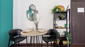 Un comedor con una mesa redonda, dos sillas negras, un espejo y una estantería con plantas.