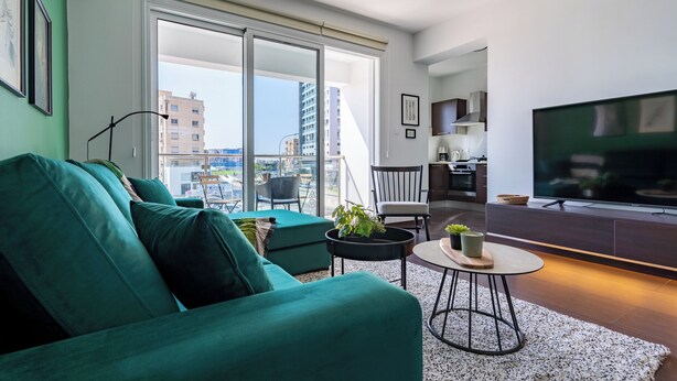 Una sala moderna con un sofá color turquesa, una mesita redonda y un televisor.