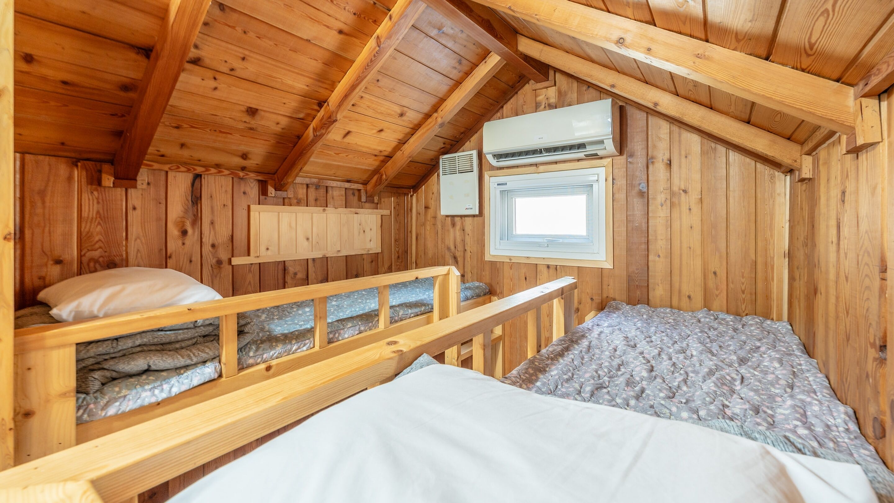 Quarto de cabana de madeira com beliches, janela e ar condicionado.