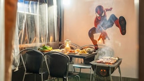 A dining area with a table set for two, a grill with meat, a salad, and a lantern.