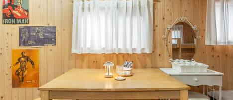 A wooden room with a table, a mirror, and a bed. There are posters on the wall and a curtain over the window.