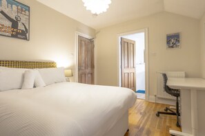 Habitación de hotel con una cama grande, un escritorio y una silla. Hay dos puertas, una que da al baño y otra al pasillo.