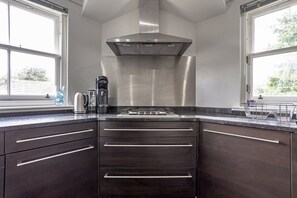 A modern kitchen with dark cabinetry, stainless steel appliances, and large windows providing natural light.