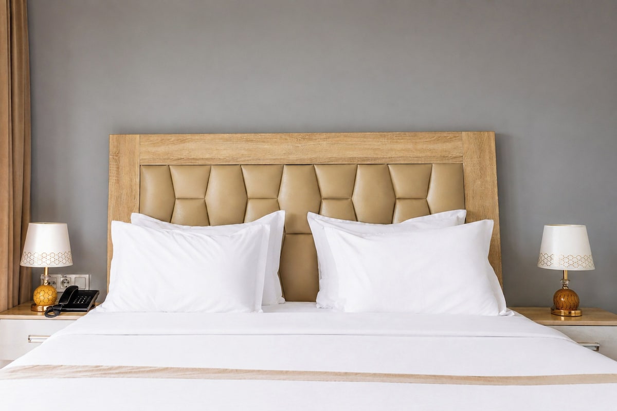 A hotel room with a wooden headboard, two white pillows, a bed with white bedding, and two bedside tables with lamps and a telephone.