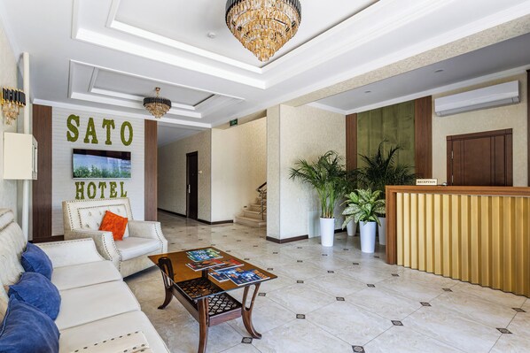 A hotel lobby with a reception desk, a sofa, a coffee table with magazines, and a chandelier.