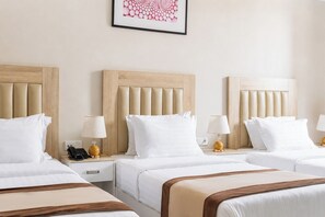 Une chambre d’hôtel avec trois lits, chacun doté d’une tête de lit en bois, de draps blancs et de lampes de chevet.